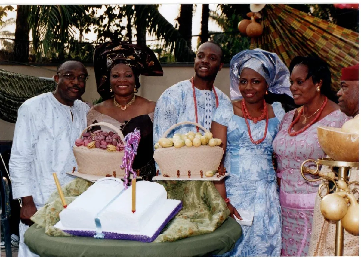 A traditional ceremony in a garden, a family gathered around baskets of yams and a white cake shaped like an open book.