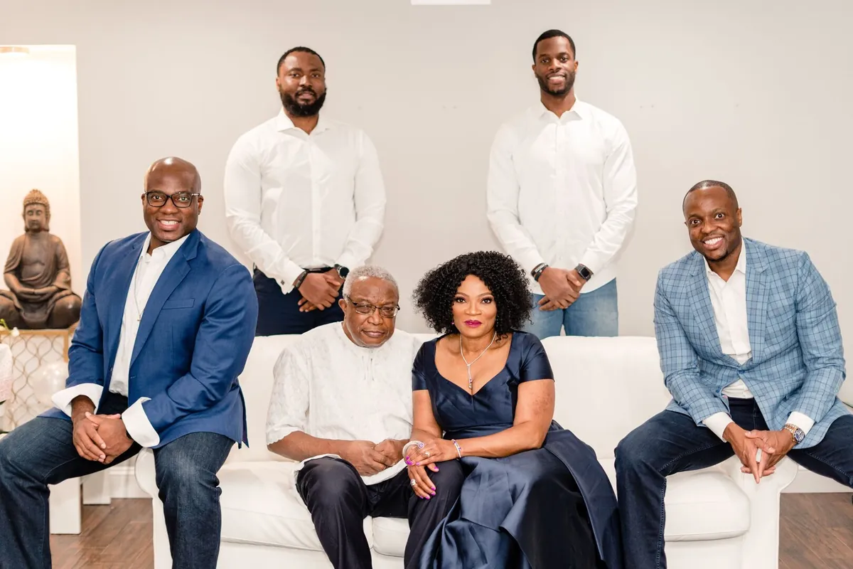 Nathan and Ify seated on a white sofa, with four younger men in blazers and white shirts around them.