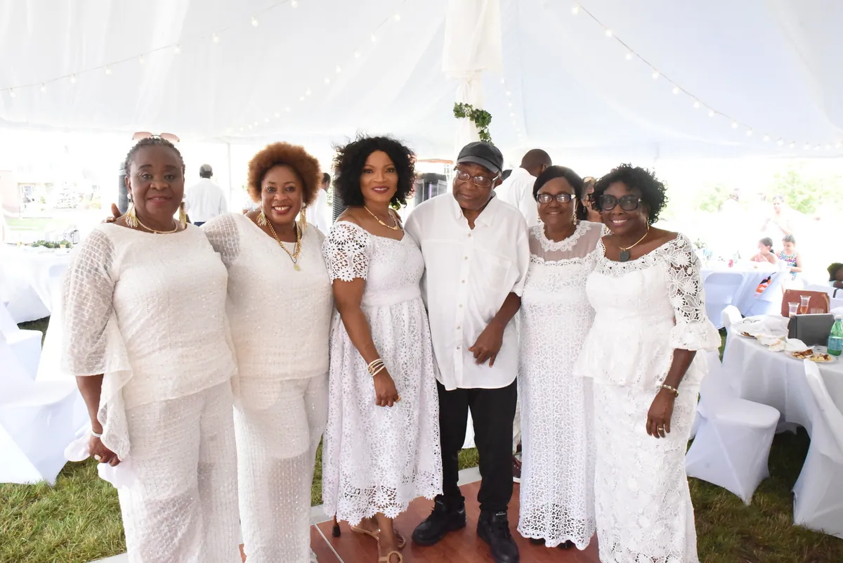 Nathan standing among a group of women dressed in white at an outdoor celebration.