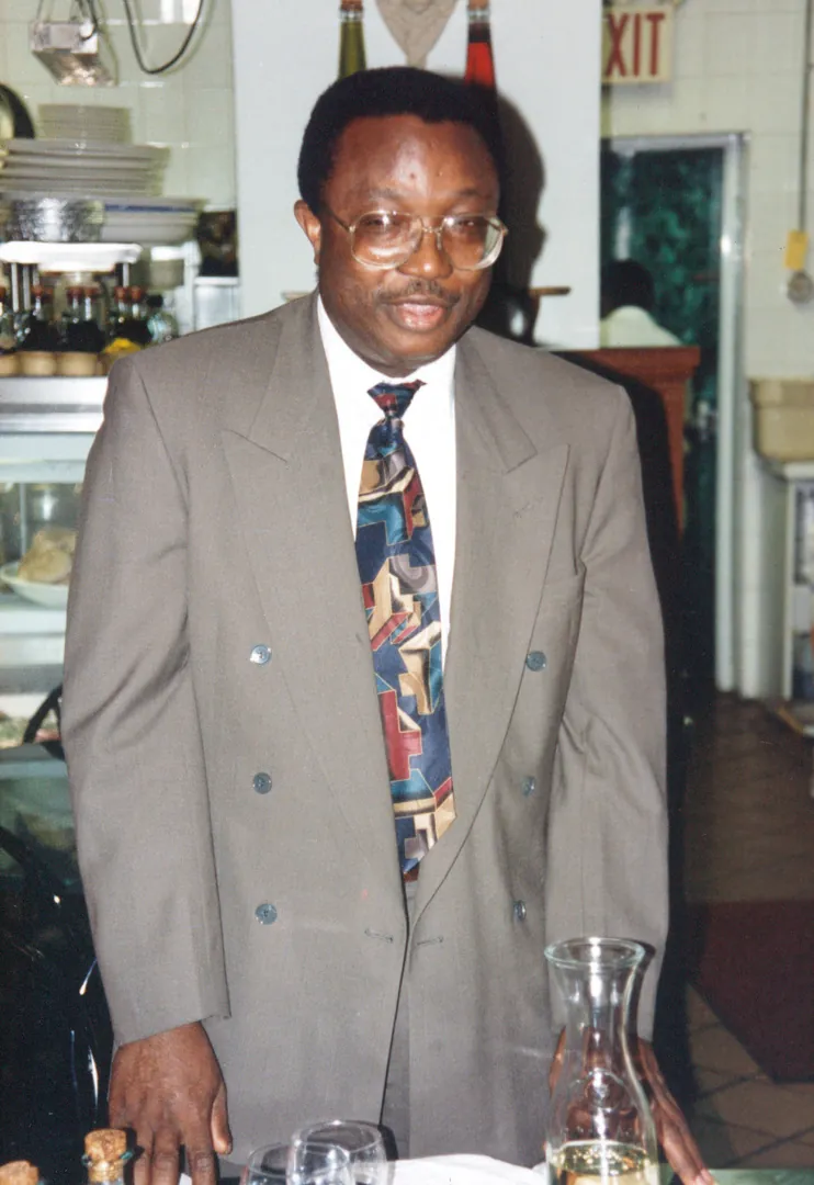 A man in a gray suit and a colorful tie standing at a table in a restaurant.