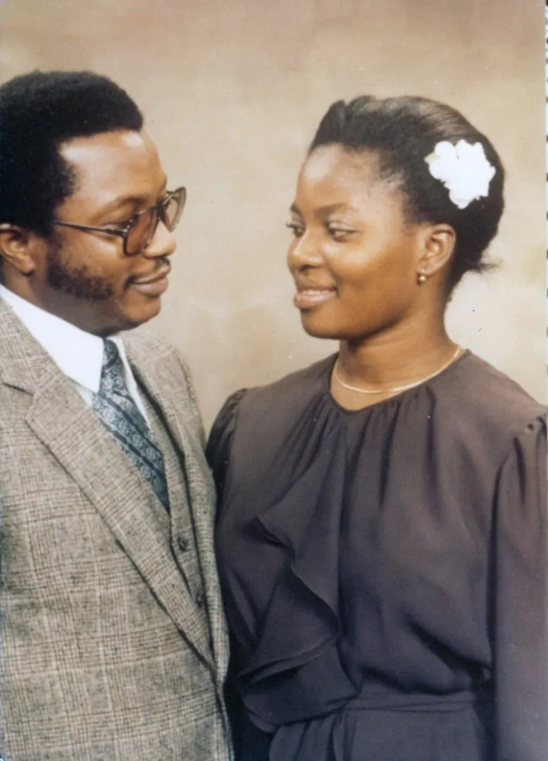 A young couple in a studio portrait, the man in a tweed jacket and tie looking toward the woman, who wears a white flower in her hair.